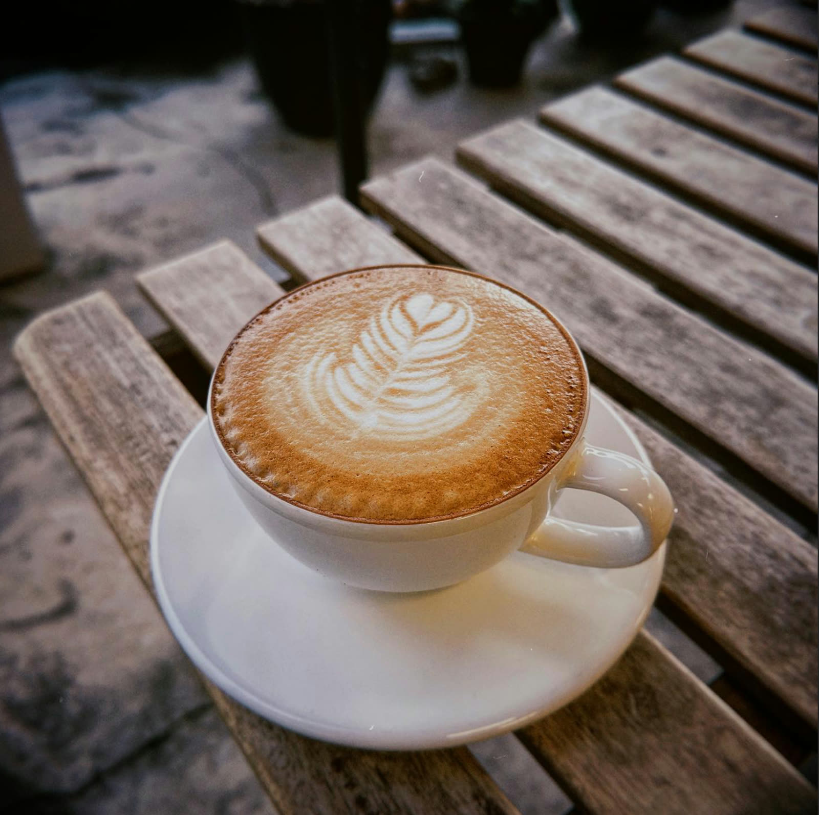 A latte with heart rosetta art in a white cup on a weathered wooden table at Kafe Tuju