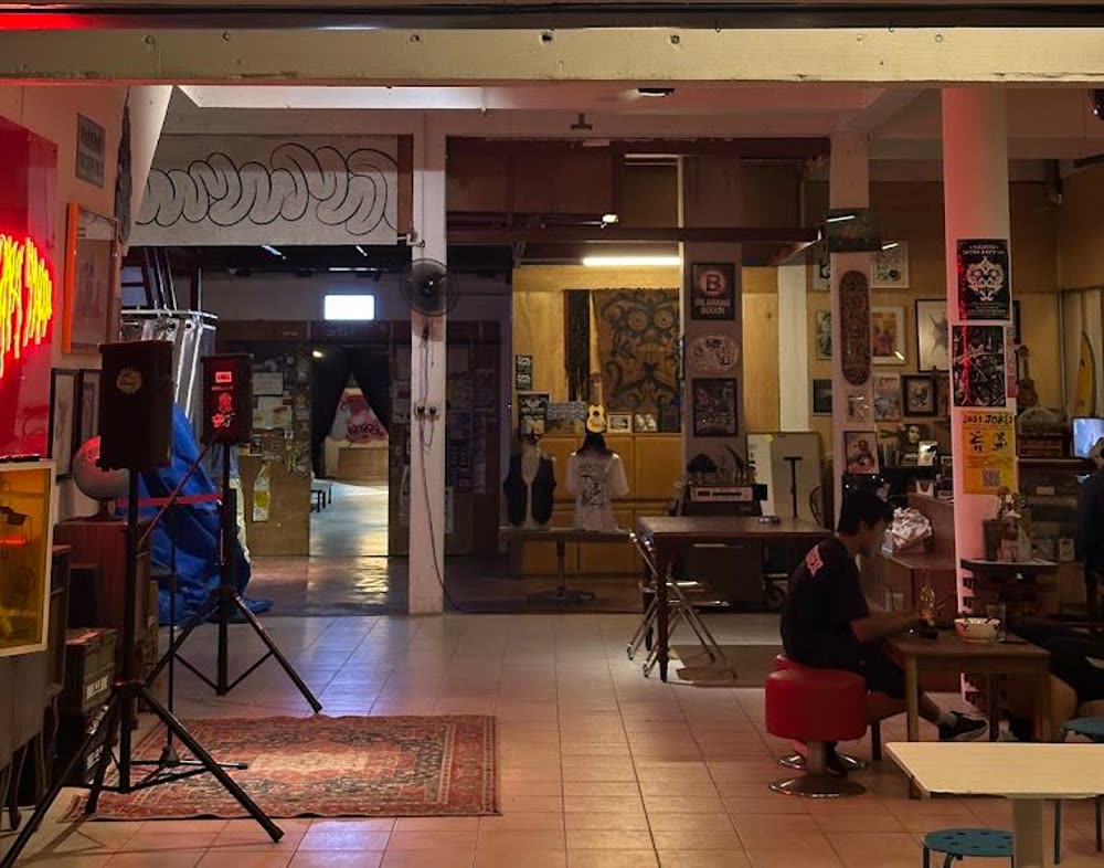 The main room at Kafe Tuju with a PA speaker, neon sign, art prints on the walls and customers seated at tables