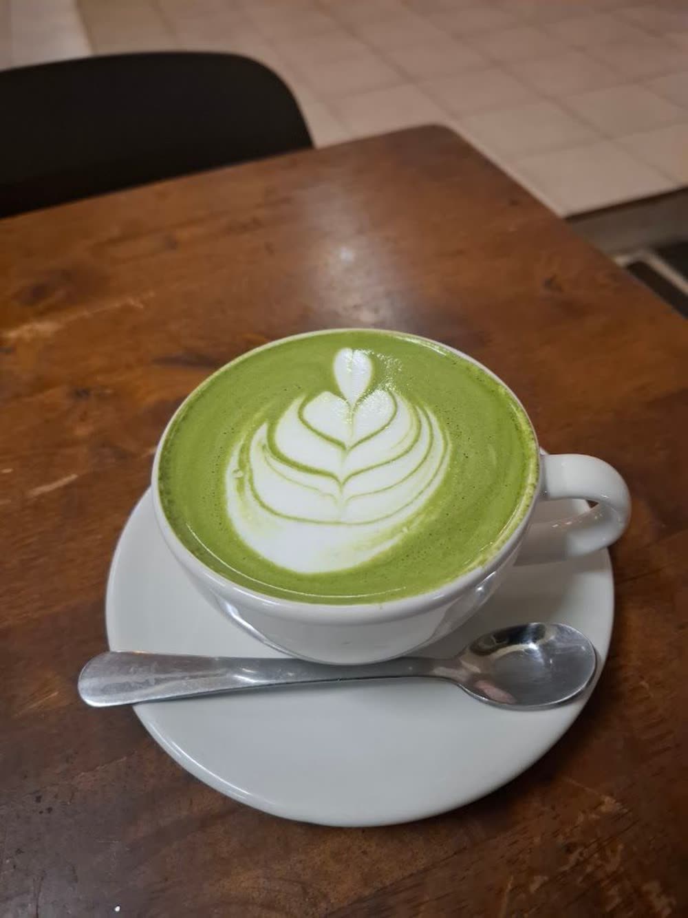 Matcha latte with rosetta art in a white cup on a dark wooden table