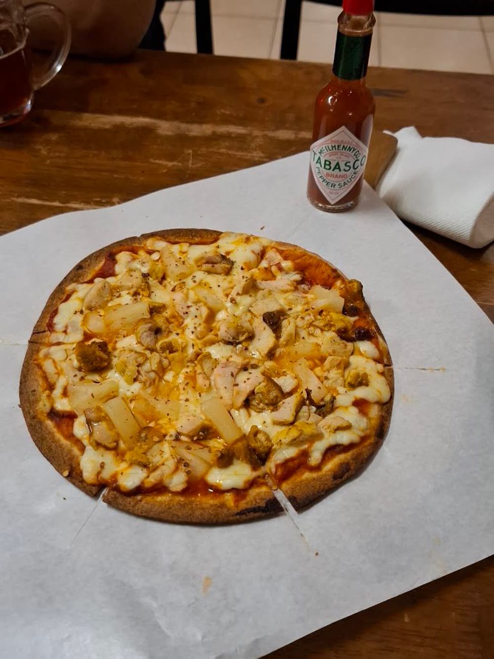 Thin crust pizza served on paper with a bottle of hot sauce alongside